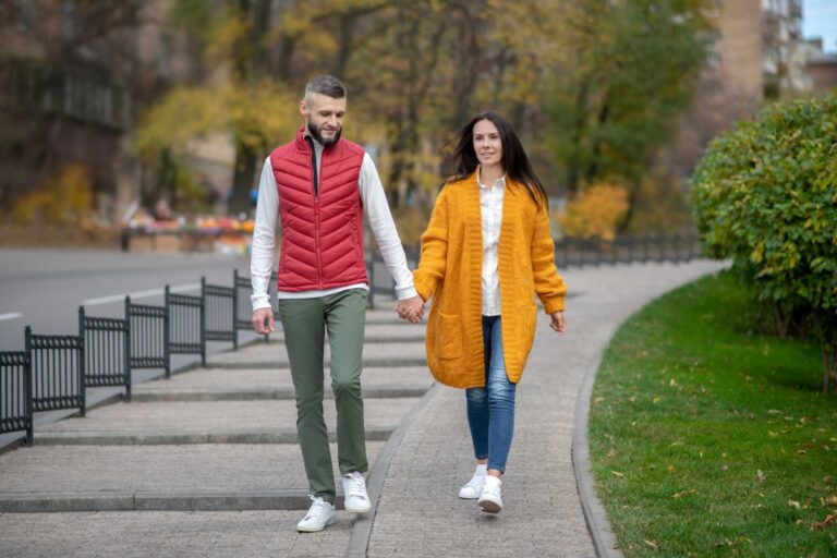 A smiling man and woman walking down the street together while holding hands.